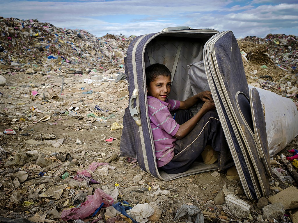 A boy takes a break from sorting recyclables inside a suitcase to protect himself from the high winds blowing filth around. Masaya, Nicaragua. Photo by: Timothy Bouldry, 2015. 