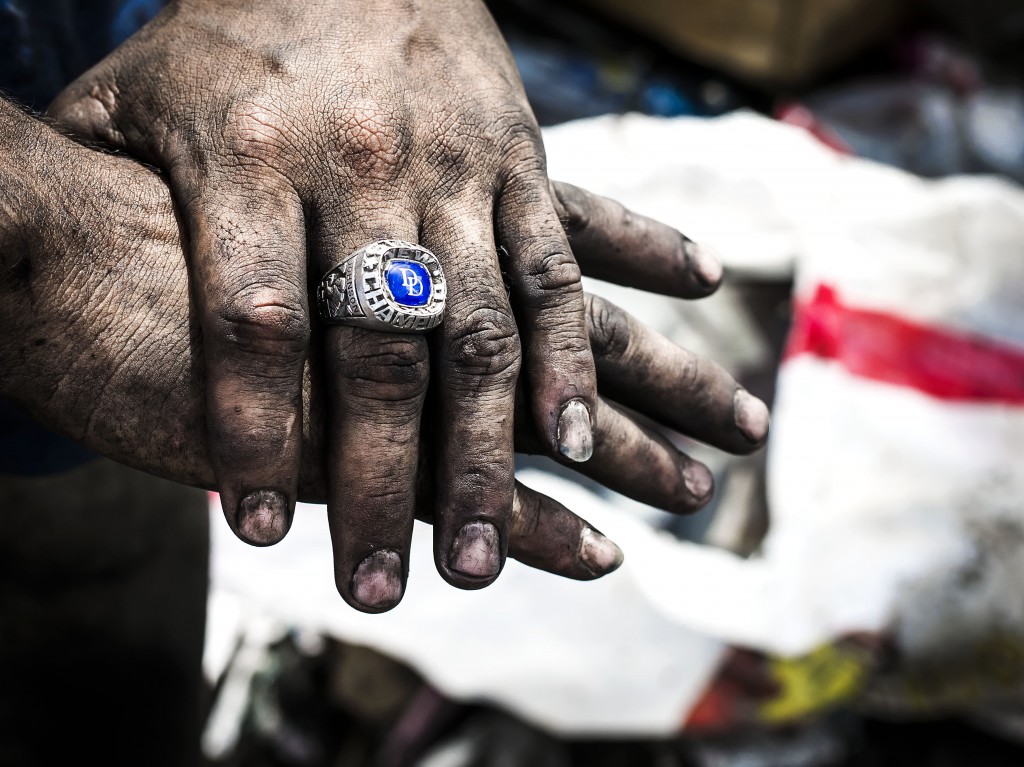 An 18 year old boy displays his dirty hands and a school ring he found from sorting garbage. He says he works here because can not find a job and cannot go to school because he has no home. He sleeps in a tiny handmade tent next the trash to wake up to first grabs of the garbage. Esteli, Nicaragua. Photo by: Timothy Bouldry, 2015.